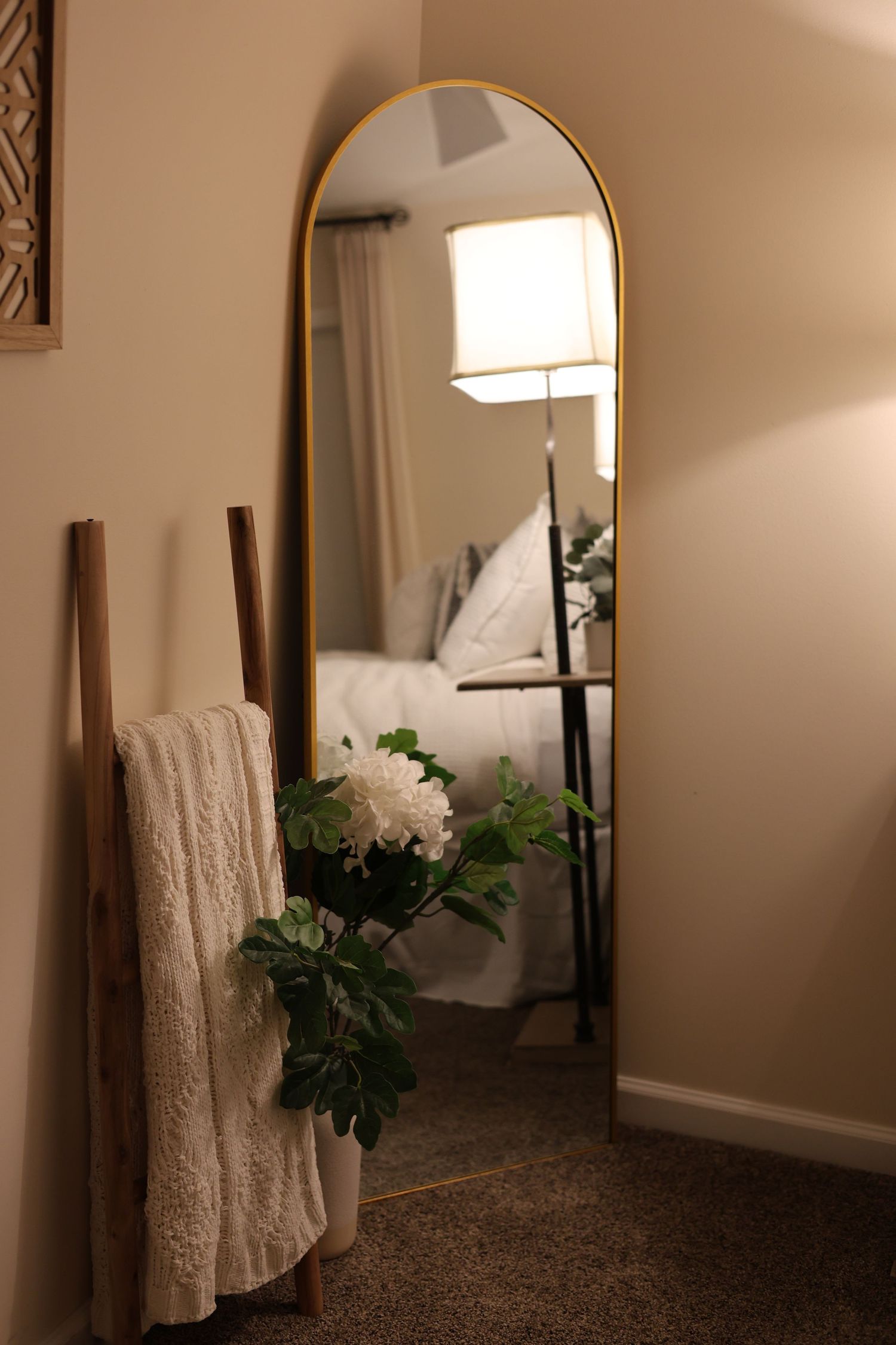 Minimalist bedroom corner featuring a rustic ladder shelf and a round accent mirror reflection in a styled Airbnb.