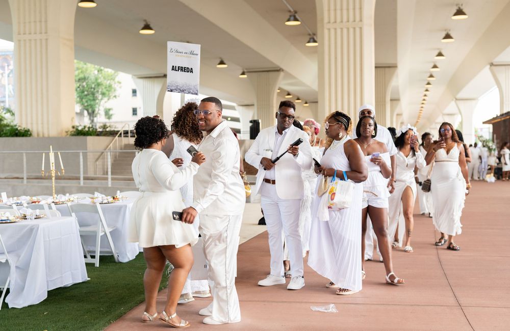Guests dressed in elegant white attire dance and celebrate at an outdoor all-white party event.