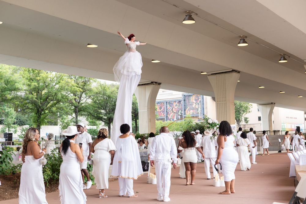 Stilt walker in white costume performs at an elegant all-white outdoor party event.