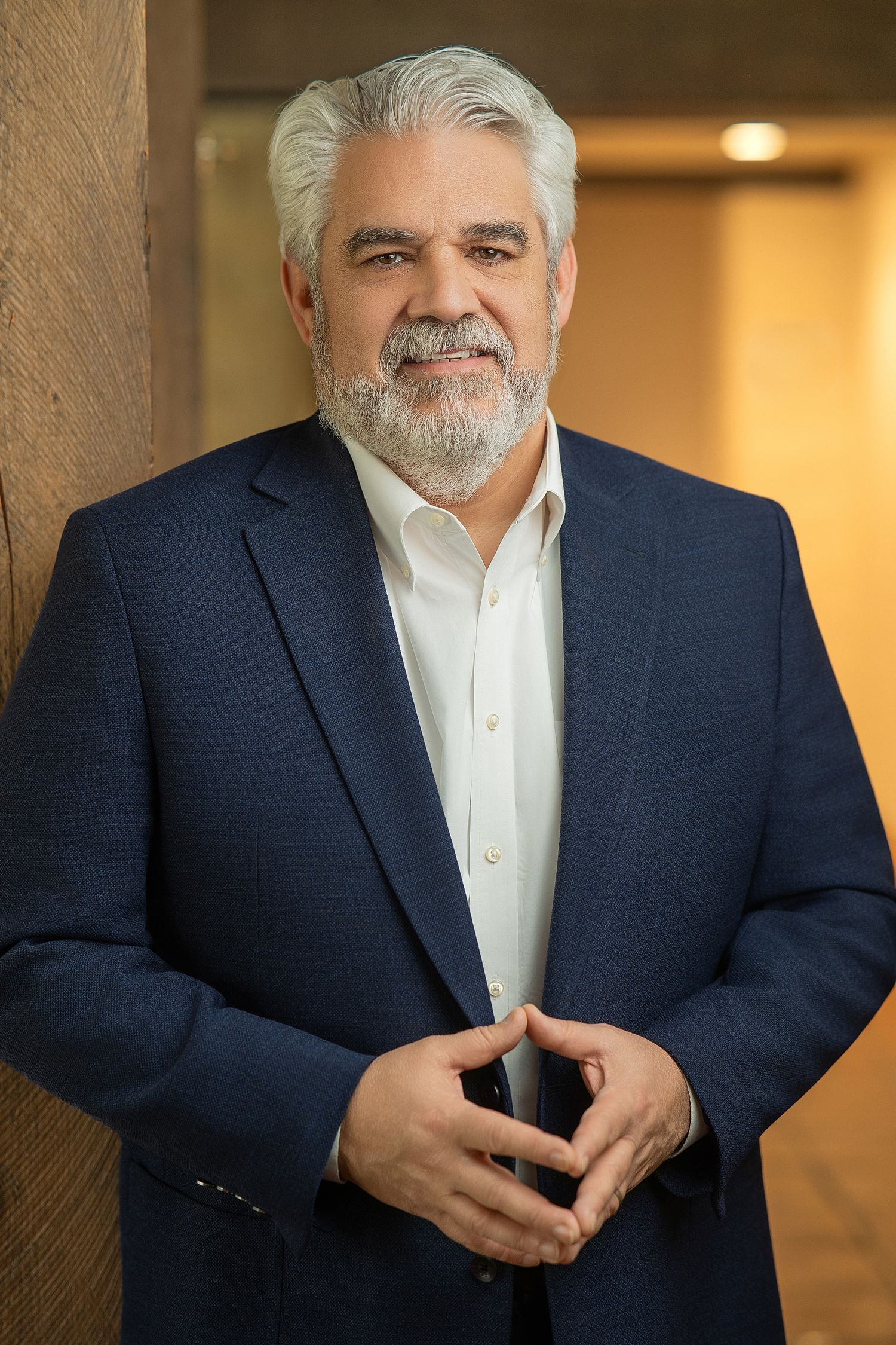 Professional headshot of a confident middle-aged man with gray hair and beard wearing a navy blue blazer.