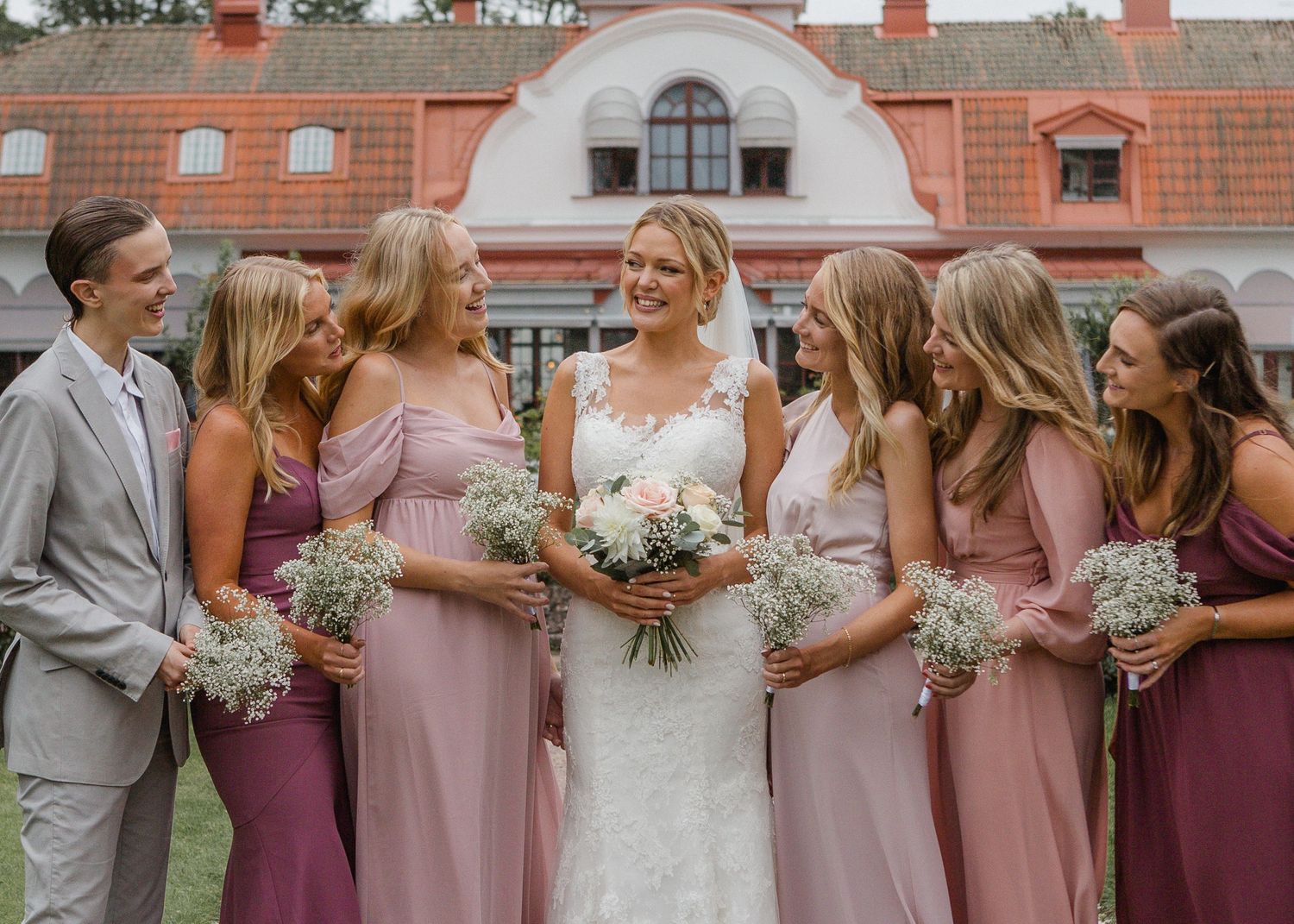 Bride with bridesmaids in pink dresses holding bouquets outside a historic manor.