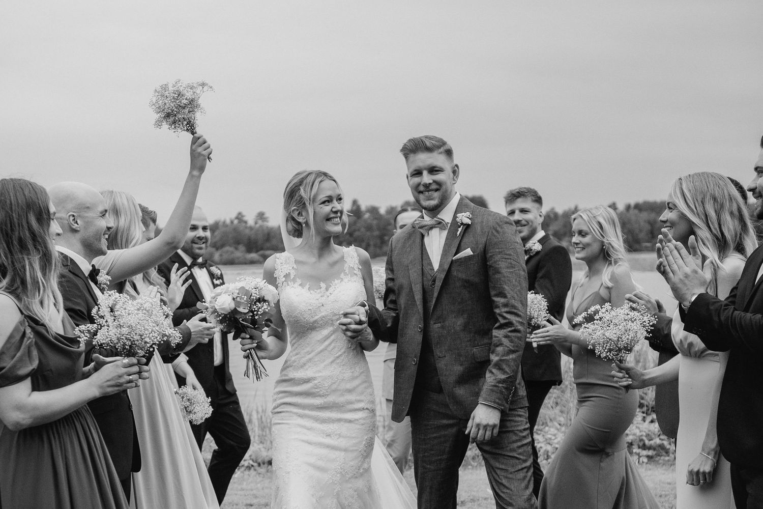 Newlyweds walk joyfully through cheering guests in a black and white wedding photo.