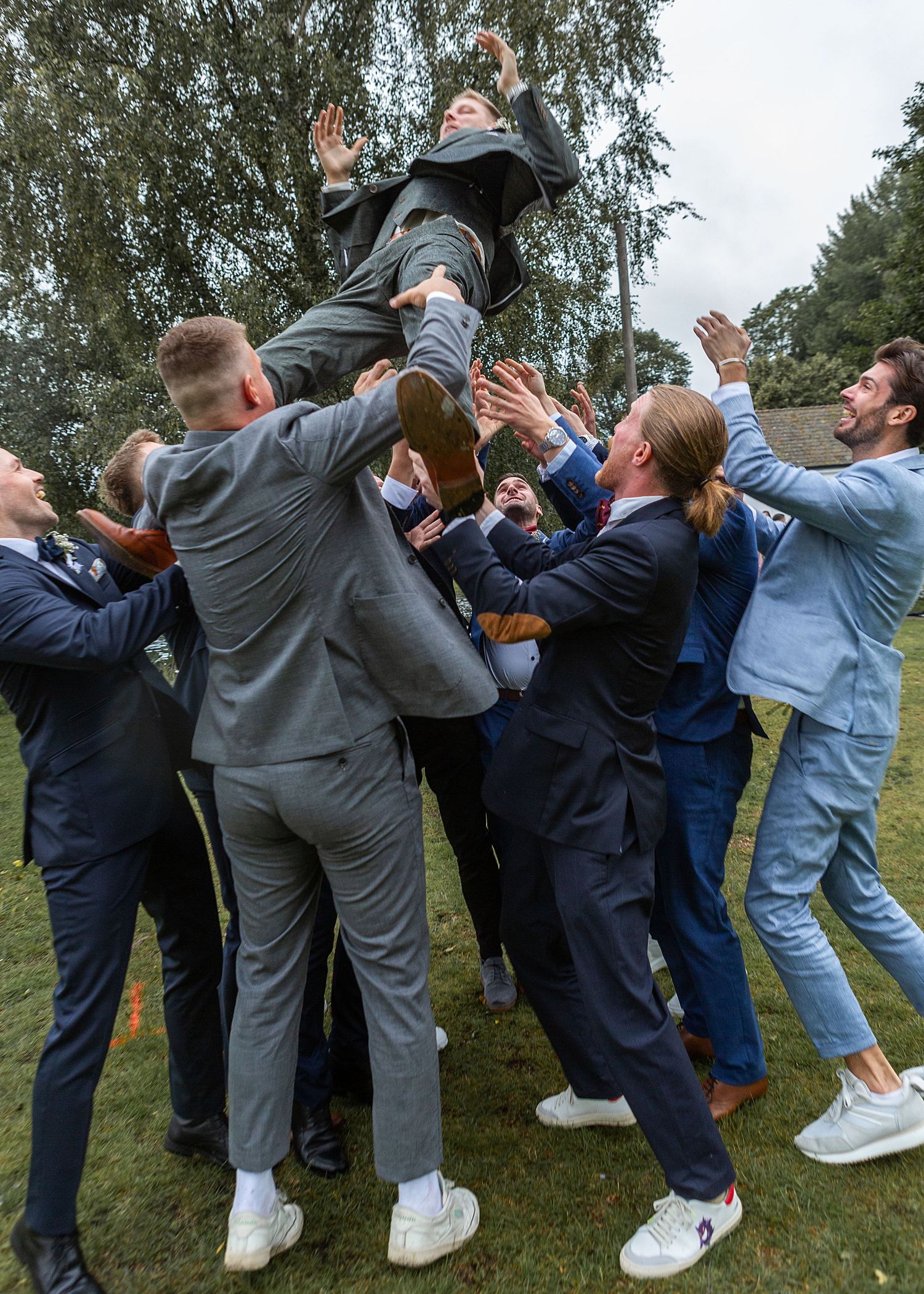 Groomsmen toss the groom into the air in a celebratory outdoor wedding moment.