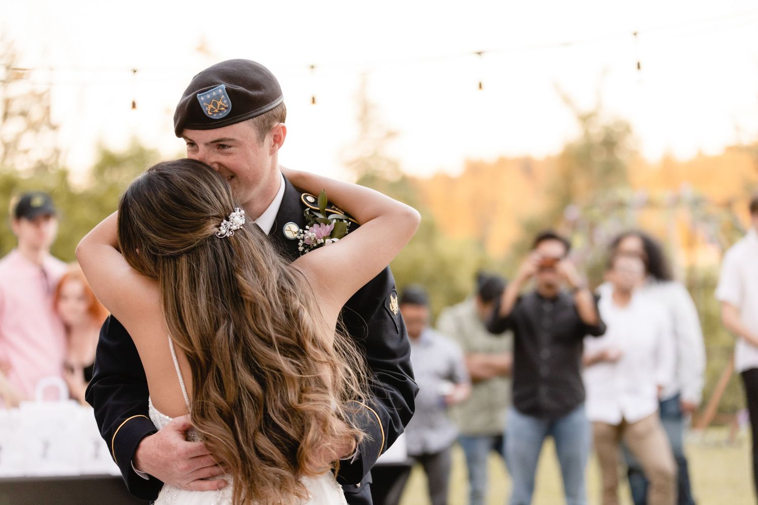 A couple dances together outdoors with guests looking on during a sunset celebration.
