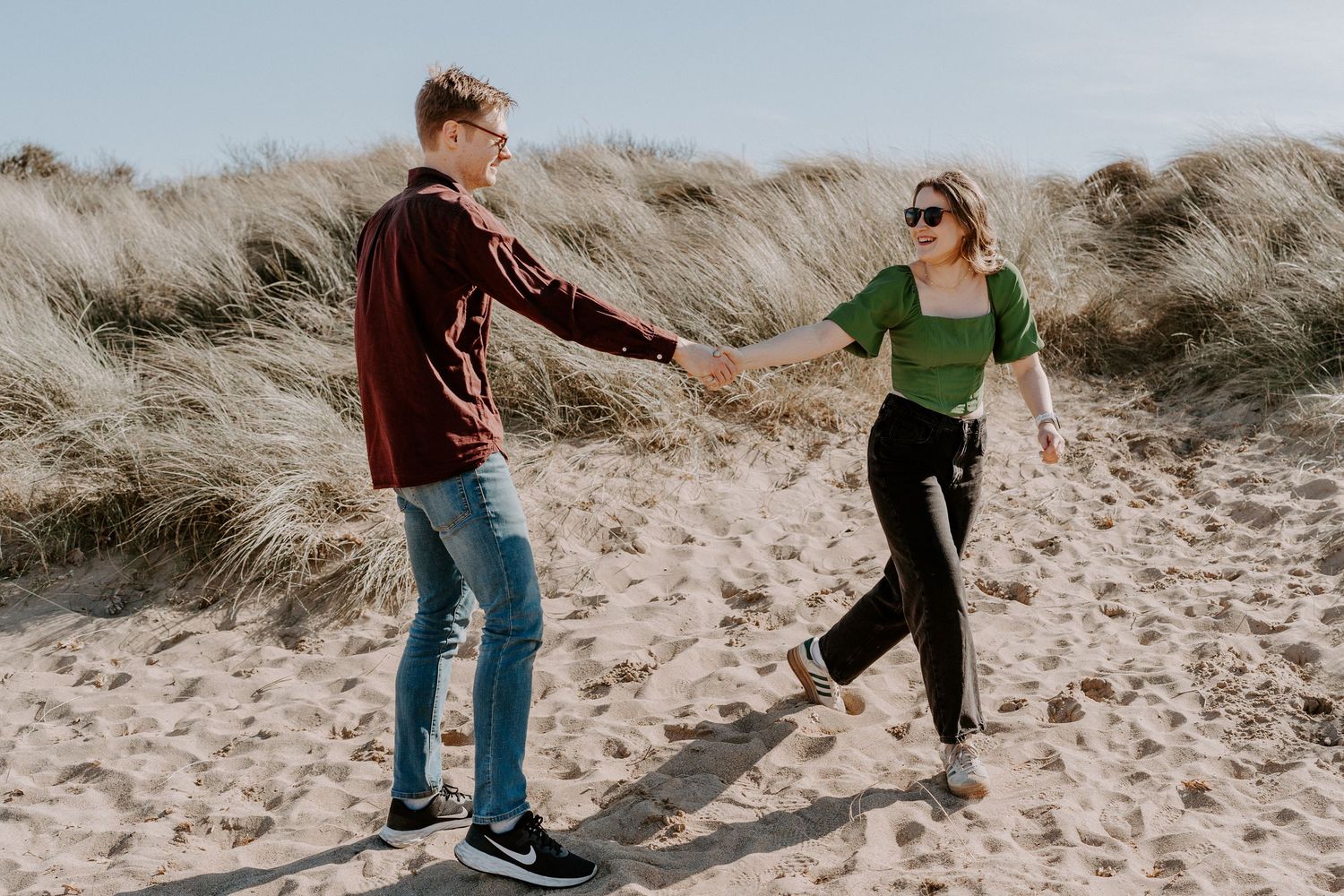A couple are dancing on the beach. They are holding hands and looking at each other and laughing.