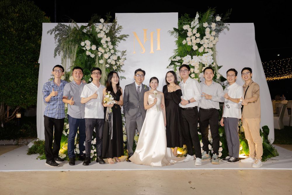 Wedding couple poses with guests in front of floral backdrop at elegant evening reception.