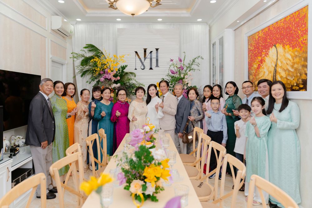 Large Vietnamese family group photo at wedding celebration indoors with floral decorations.