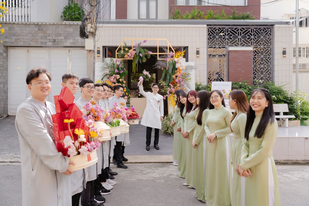 Vietnamese wedding procession with groomsmen and bridesmaids in green ao dai outside decorated home.