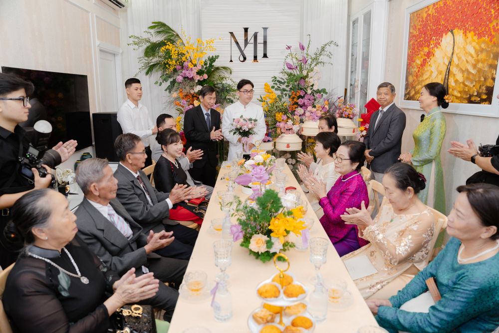 Vietnamese wedding ceremony indoors with families gathered around decorated table with flowers.