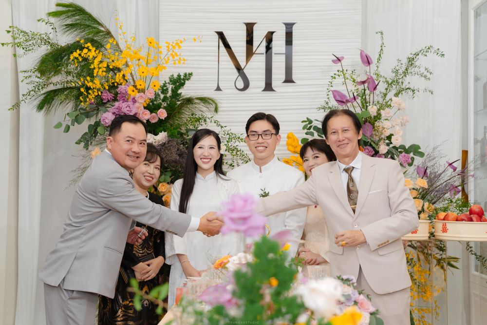 Joyful Vietnamese wedding party group photo with couple and guests at floral decorated venue.