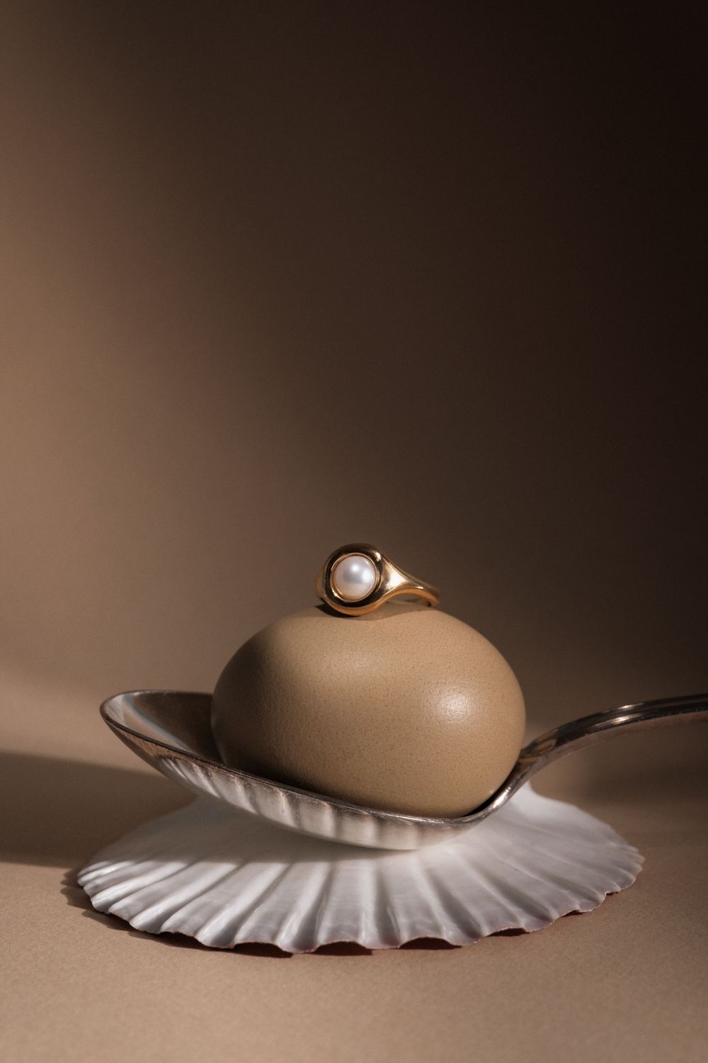 Pearl ring displayed on tan egg atop white scalloped plate in moody lighting.