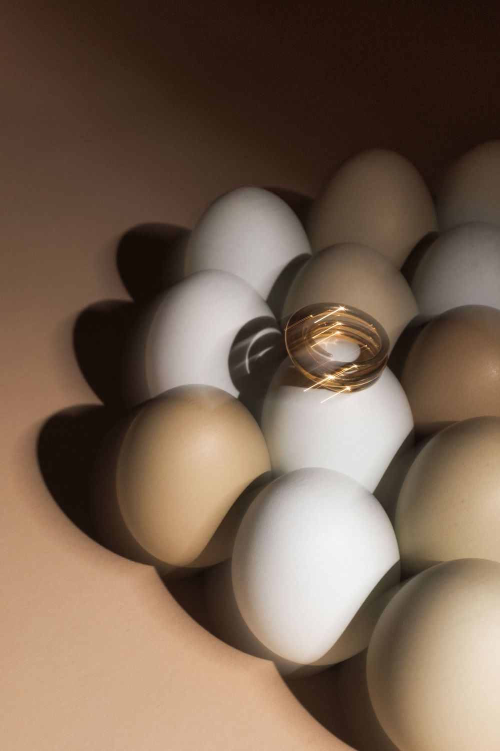 Gold spiral ring displayed among arranged white and brown eggs with dramatic shadows.