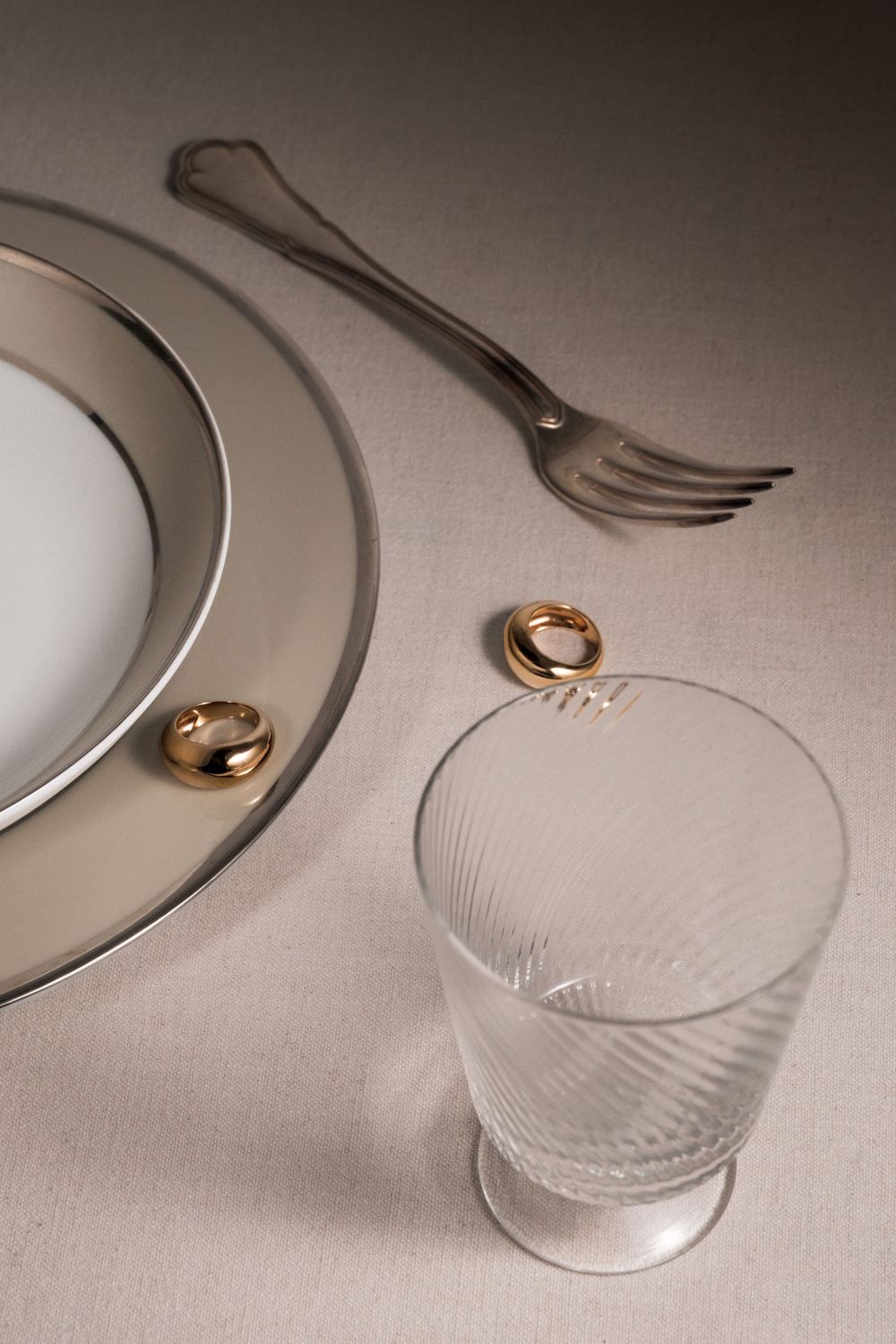 Elegant table setting with rings, crystal glass, and silverware on neutral background.