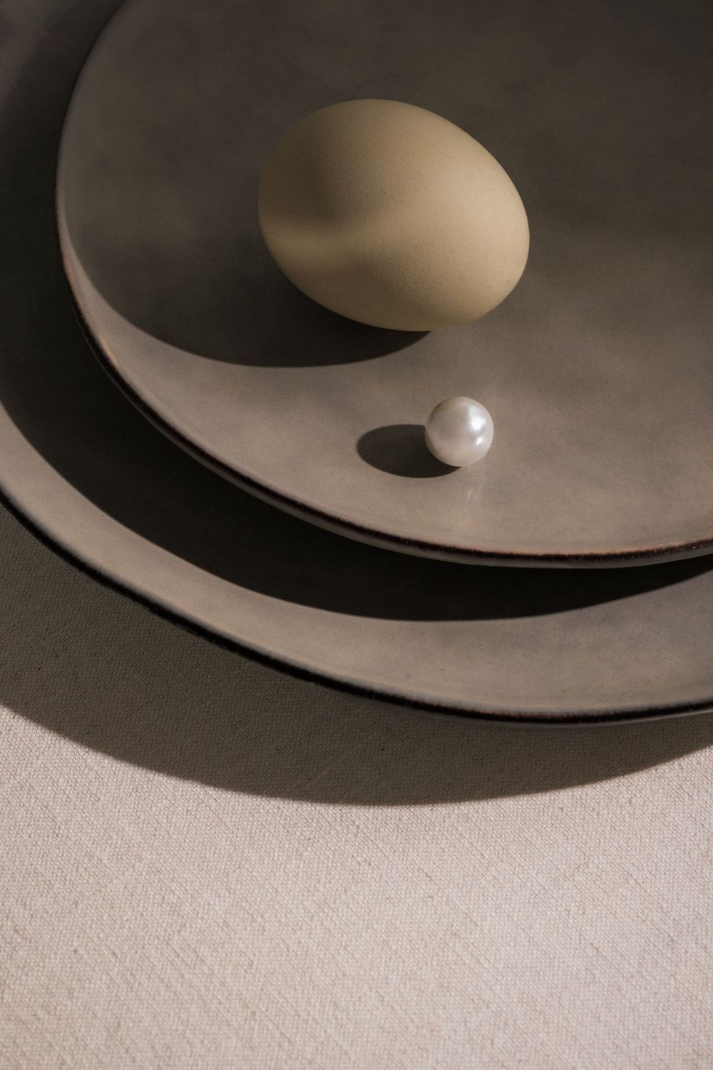 Single pearl and egg on curved black plates creating dramatic shadows.