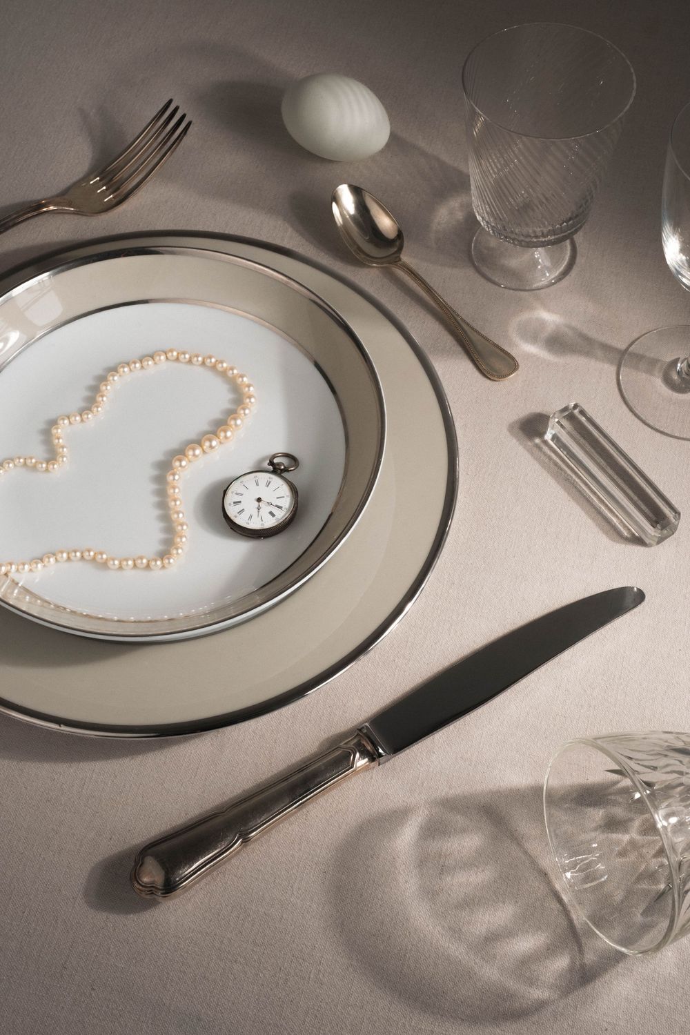 A pearl necklace arranged in a heart shape on a white plate with elegant table settings.