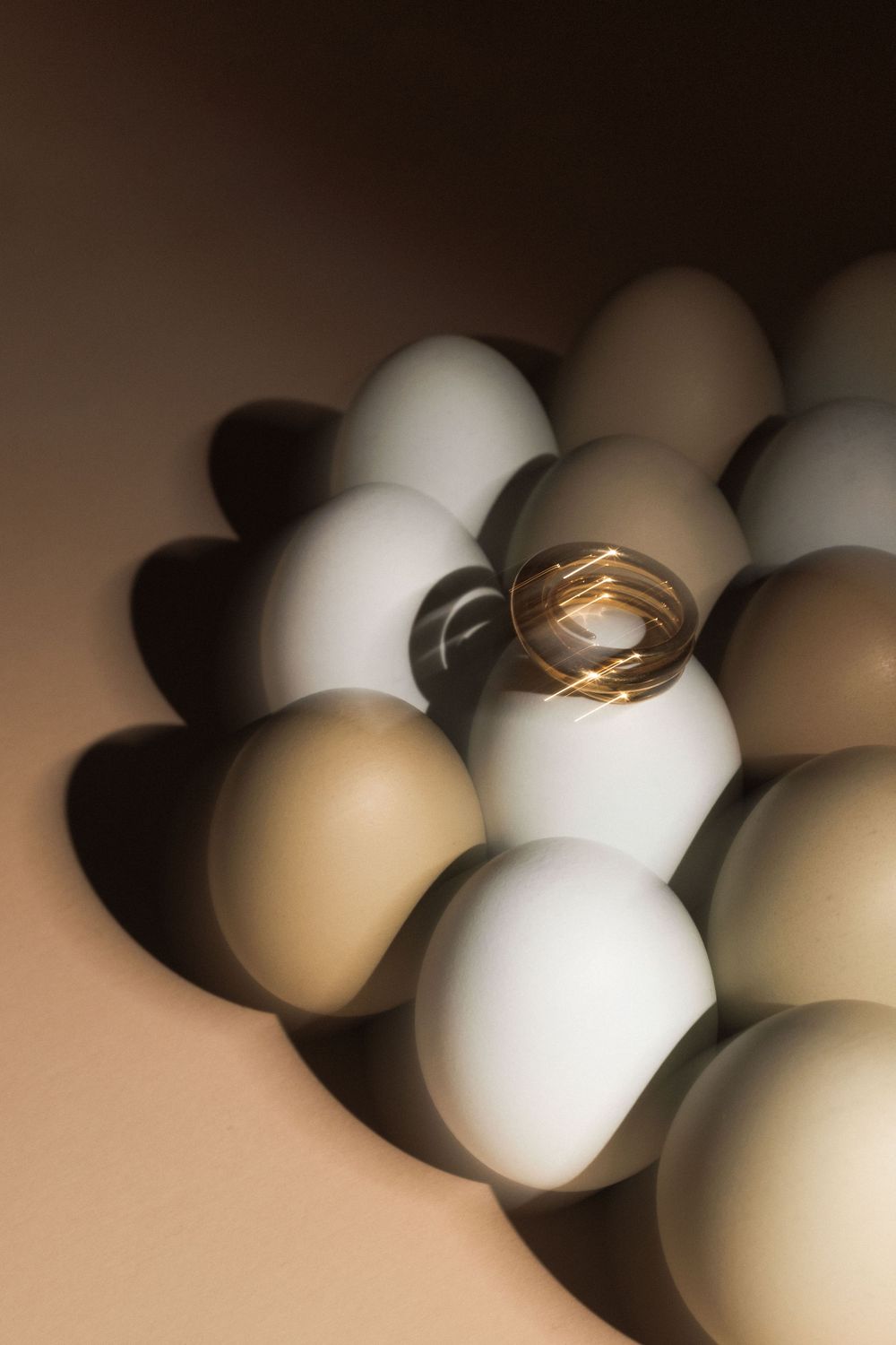 Gold wedding rings placed on top of white and brown eggs creating dramatic shadows and contrast.