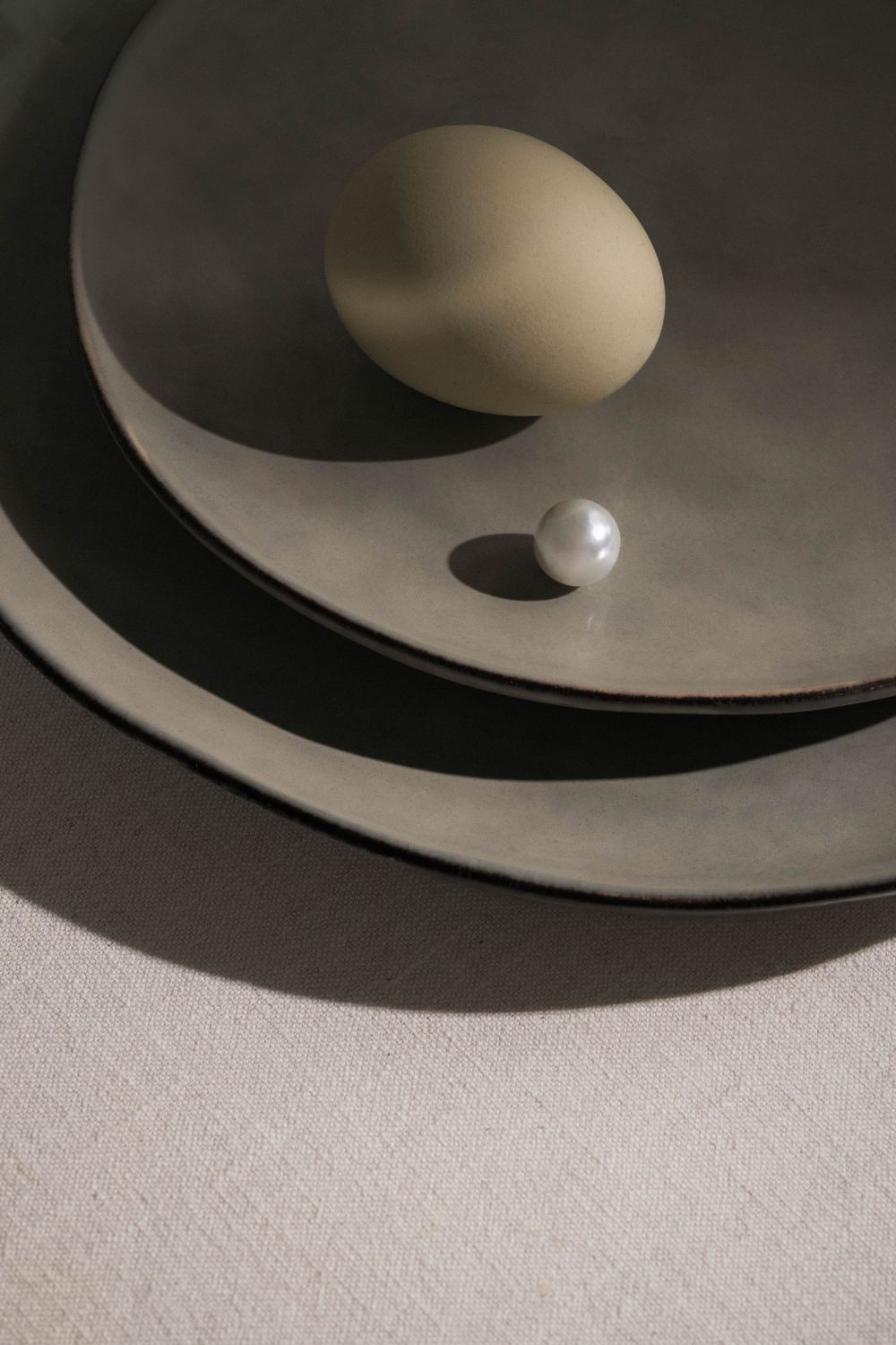 Minimalist still life with white egg and pearl on curved geometric surfaces casting dramatic shadows.