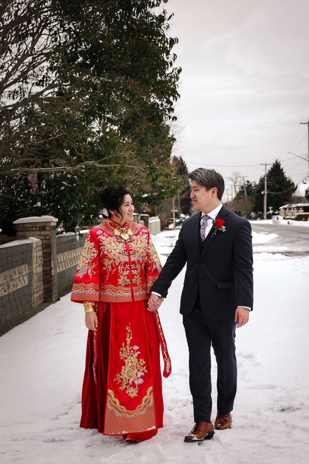 Couple in winter wedding attire featuring traditional red Chinese dress and black suit walking together in snow.smilein wedding photography