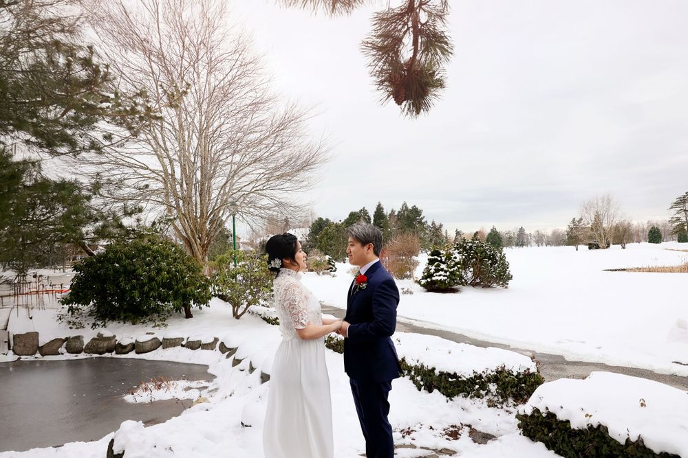 A couple stands in front of a snowy winter landscape with a frozen pond and evergreen trees. smilein wedding photography vancouver