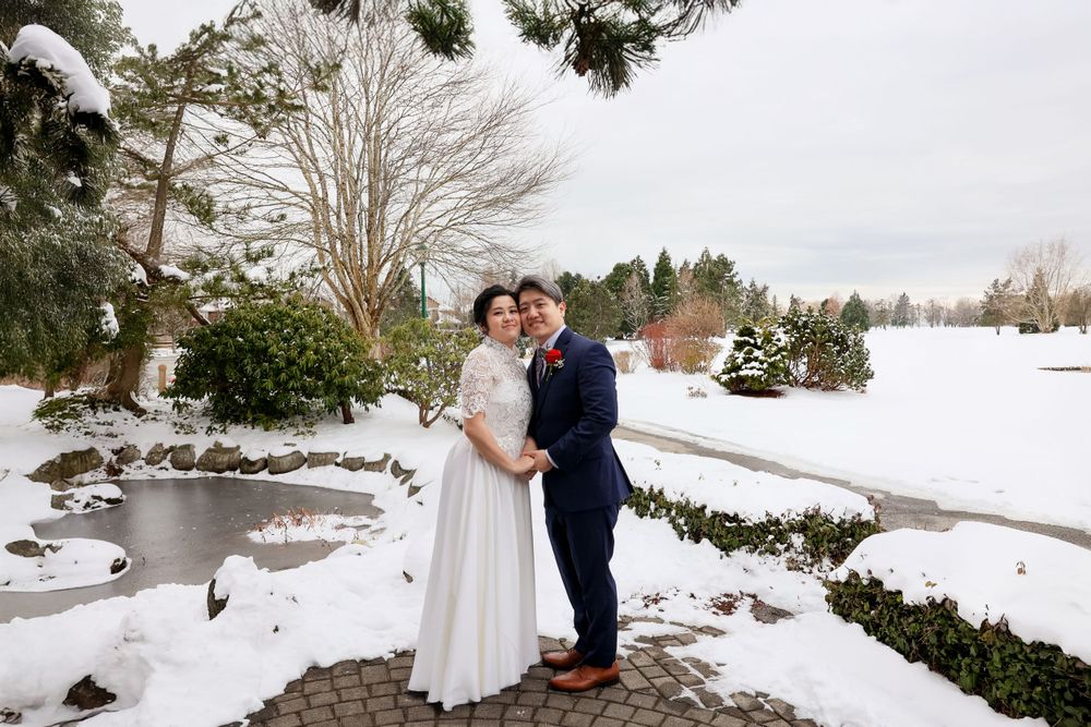 Two people in wedding attire embrace on a snowy winter day beside a frozen pond. smilein wedding photography vancouver