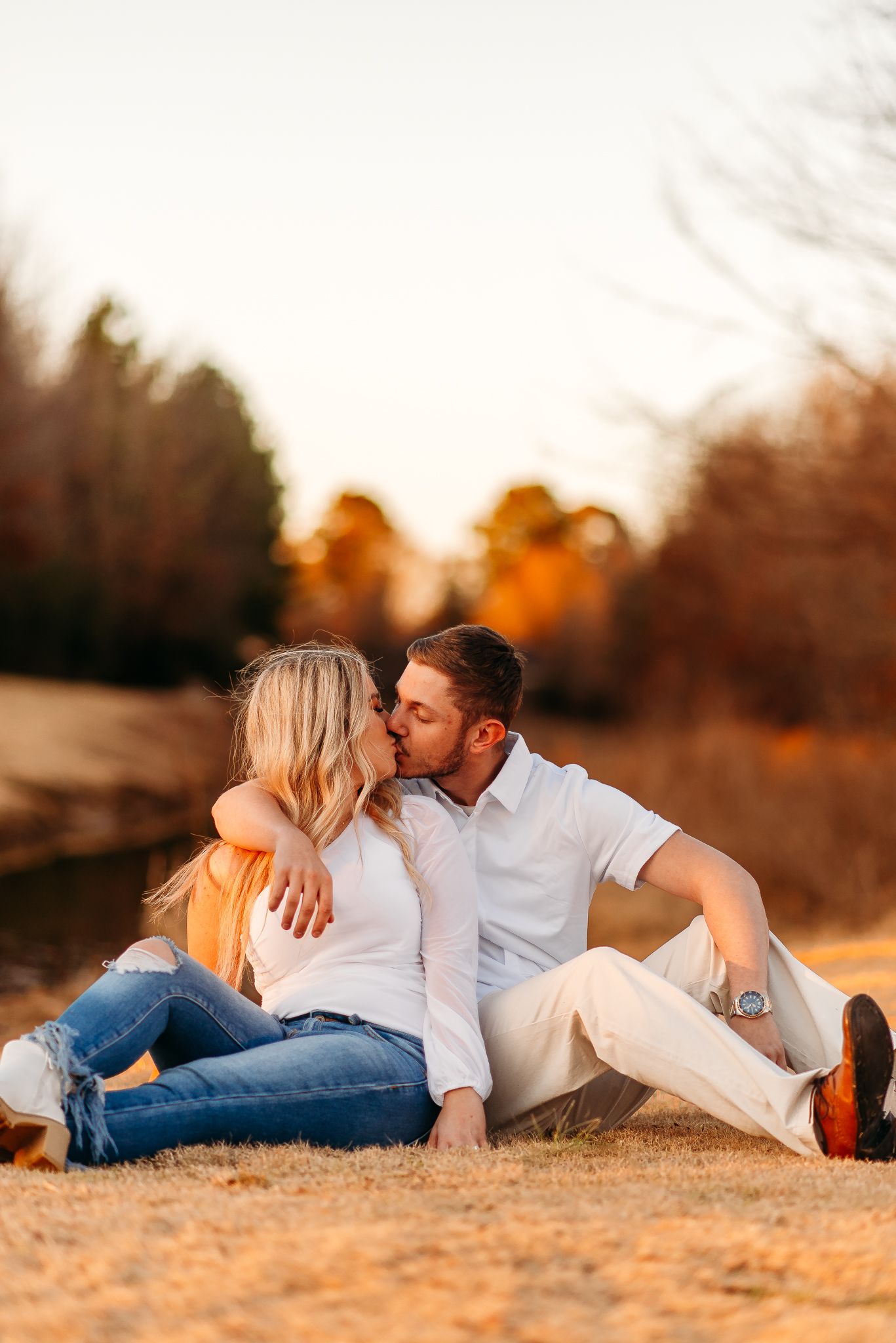 Intimate couple embracing on ground during golden hour sunset photoshoot.