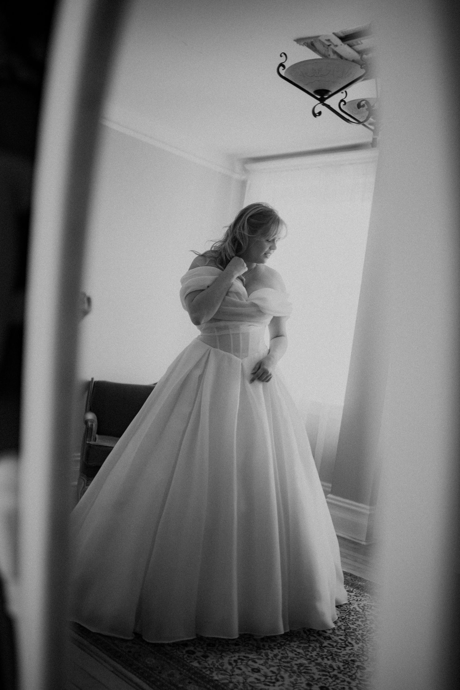 Black and white mirror reflection of bride in a full ballgown wedding dress with off-shoulder sleeves.