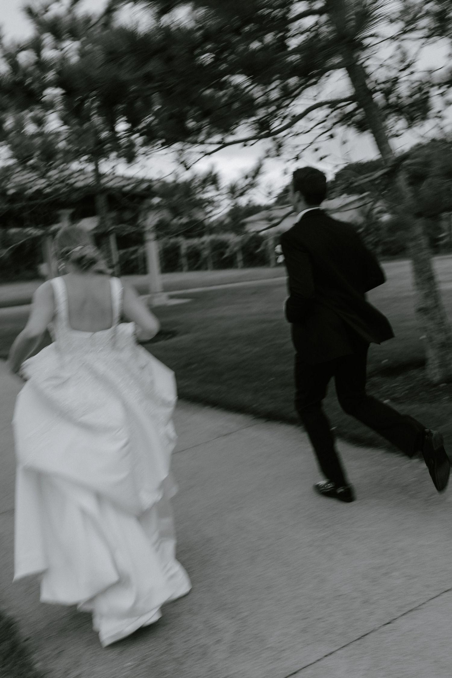 Motion-blurred black and white photo of couple running on sidewalk near vineyard during sunset photos.