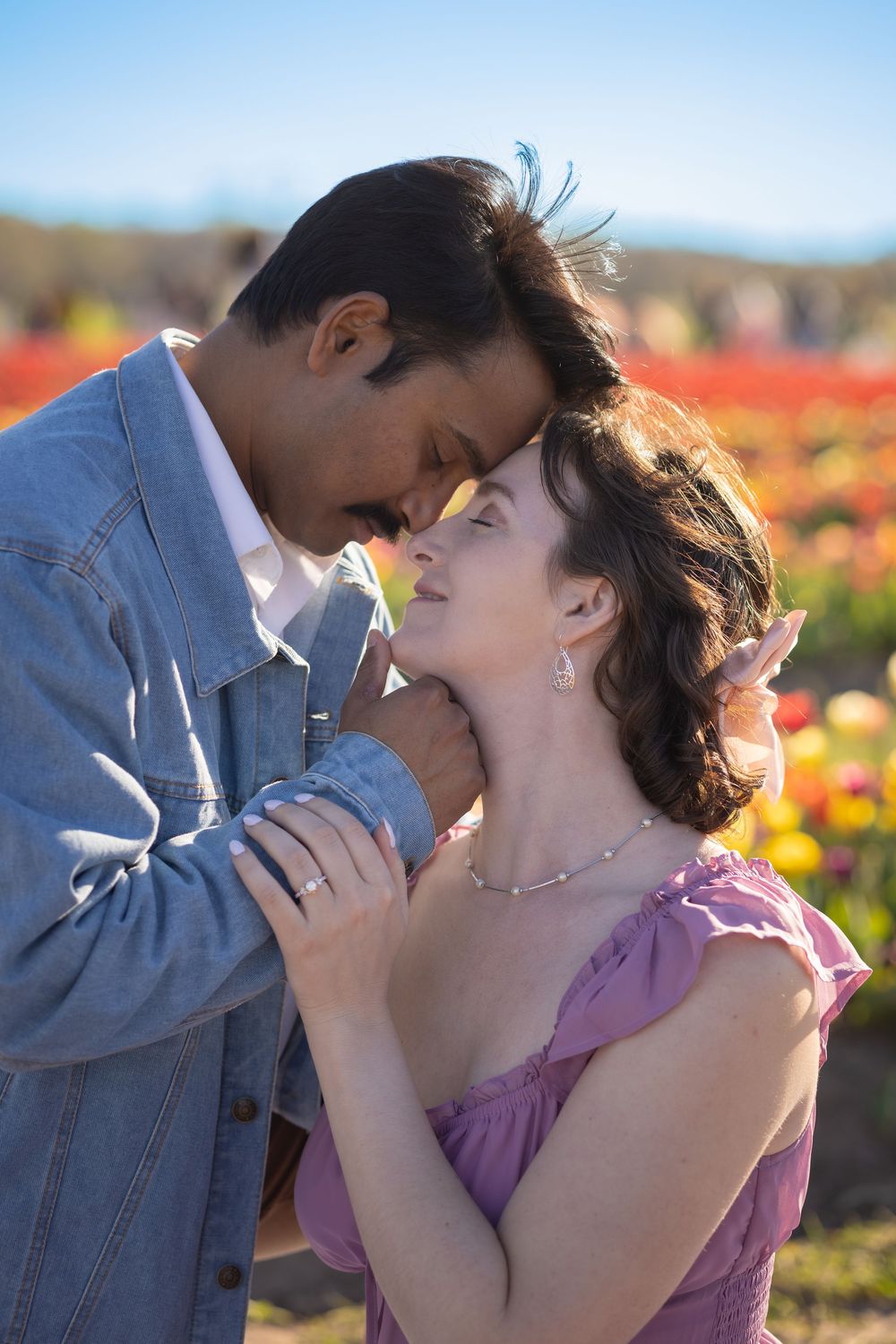 Romantic couple sharing an intimate moment in a colorful tulip field, man in denim jacket tenderly holding woman in pink dress.