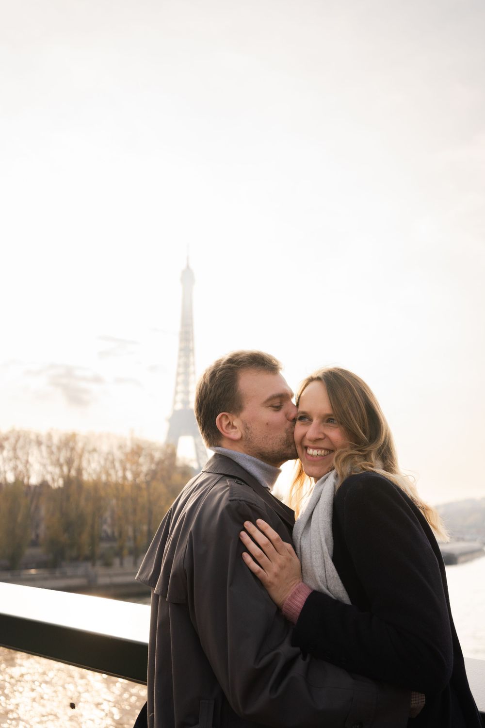 A romantic couple embraces and shares an affectionate moment with the Eiffel Tower visible in the background in Paris.