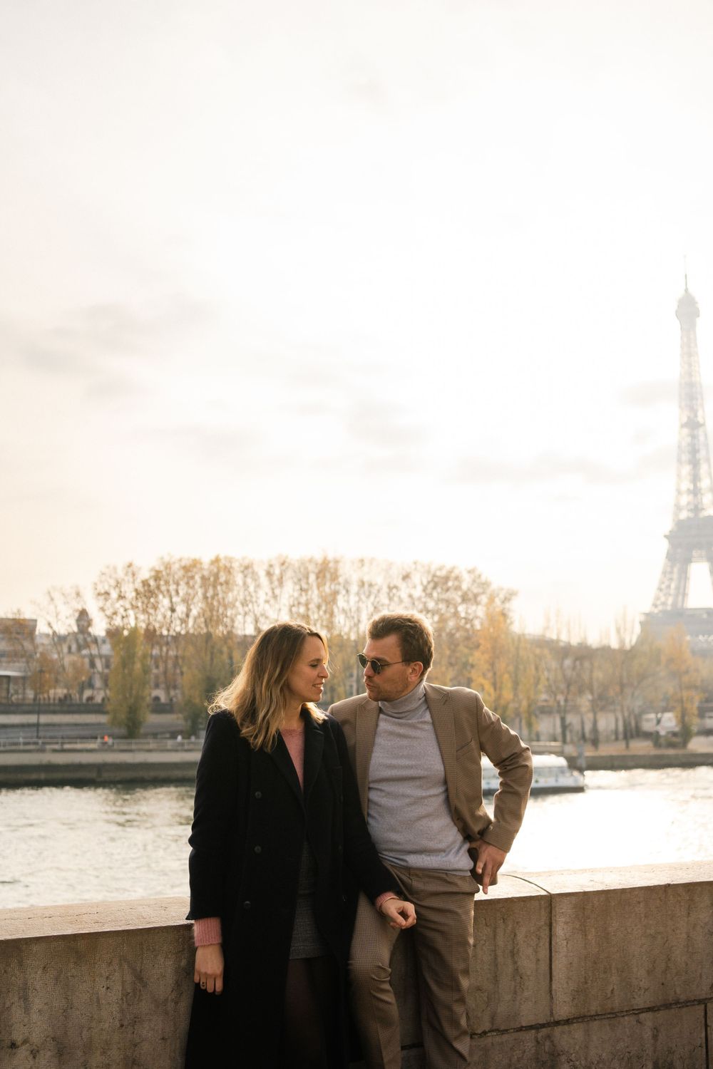 A couple shares a romantic moment overlooking the Seine River with the Eiffel Tower in the background on a cloudy Paris day.