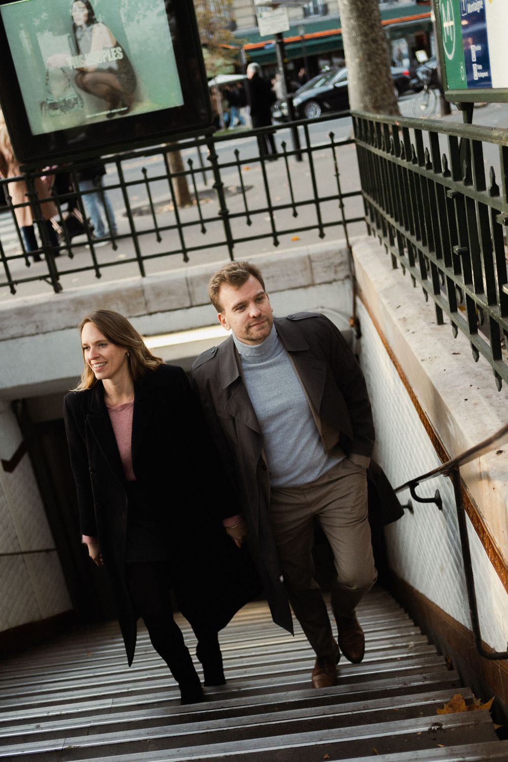 Two people in winter coats climbing concrete subway stairs in Paris.