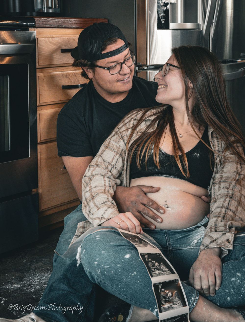 Expectant couple shares intimate moment in kitchen while holding maternity ultrasound picture.