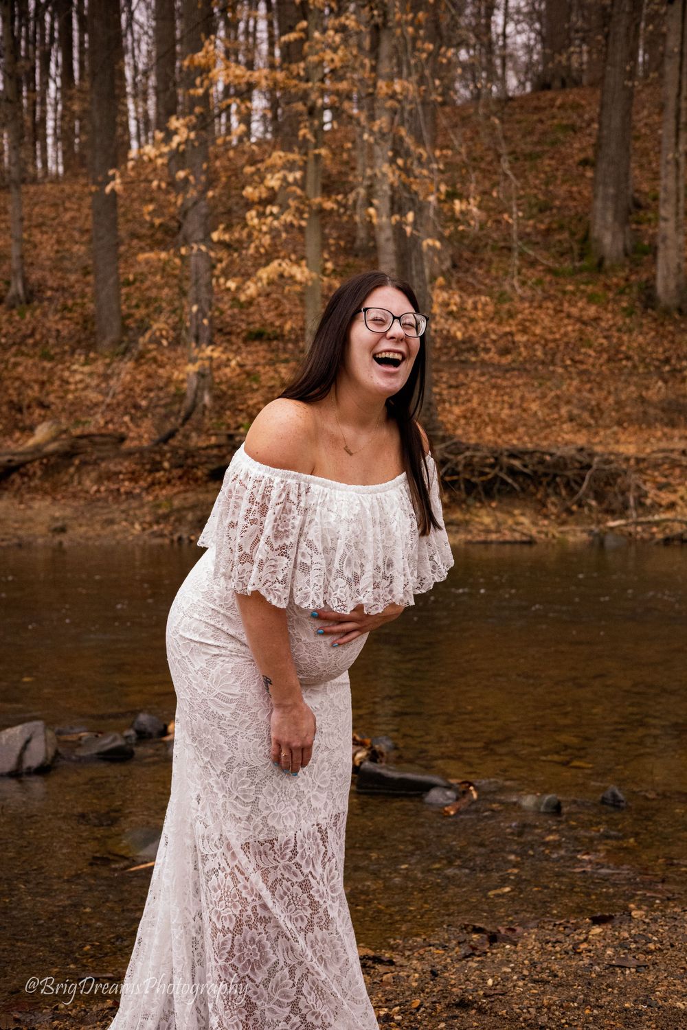 Beautiful lace wedding dress photographed near an autumn stream with fall foliage in the background.