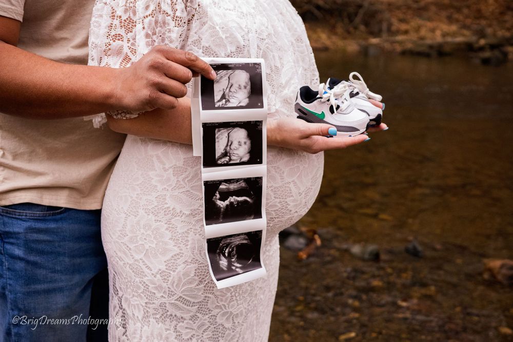Hands holding ultrasound images next to tiny baby shoes.