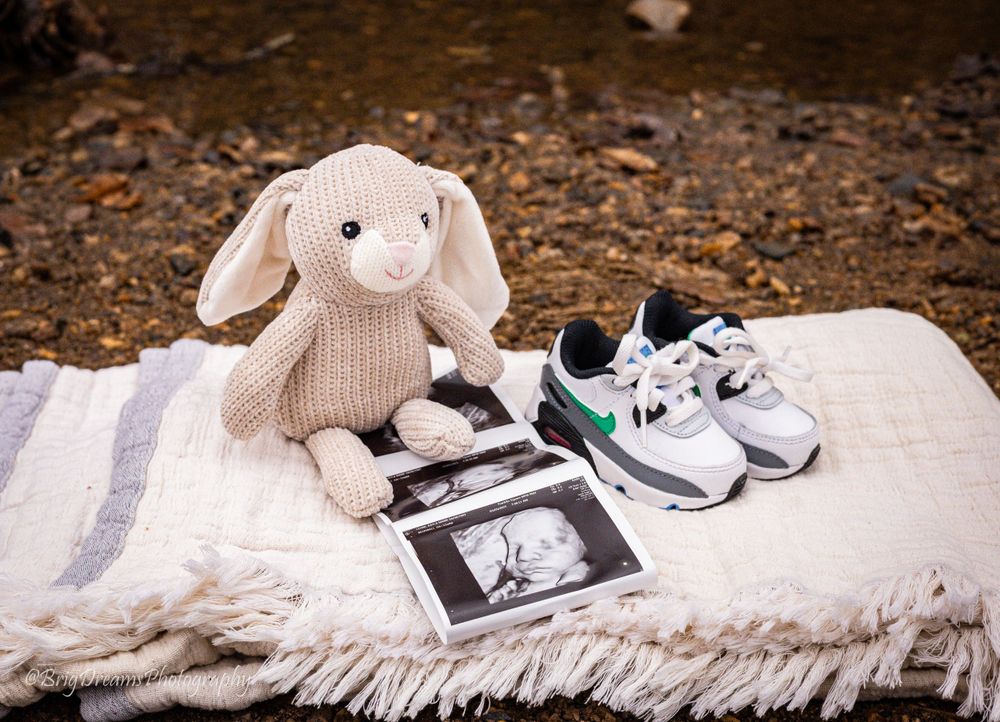 Plush bunny and baby shoes arranged with ultrasound photos on a blanket.