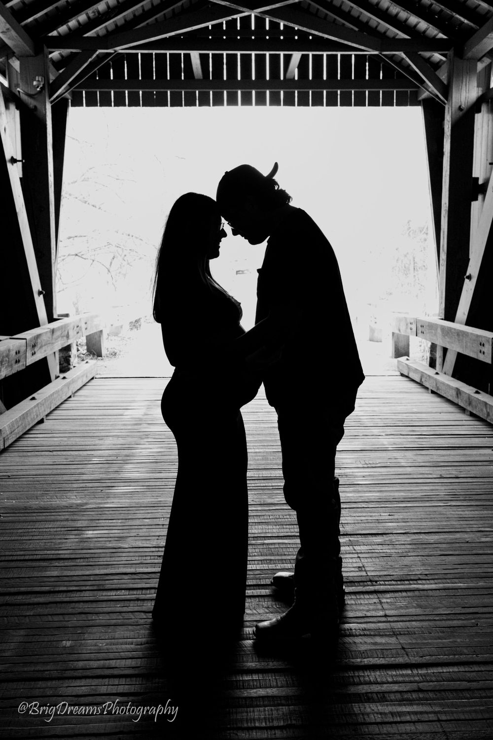 Silhouetted couple stands face to face in a covered bridge during maternity photoshoot.