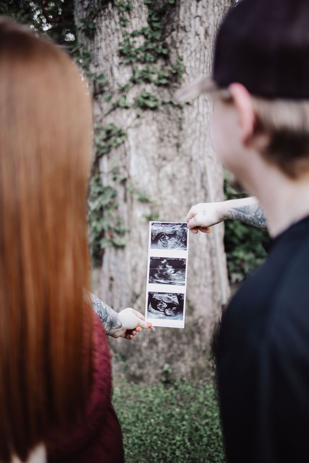 A couple holds up ultrasound photos in a series of outdoor shots against a tree backdrop.