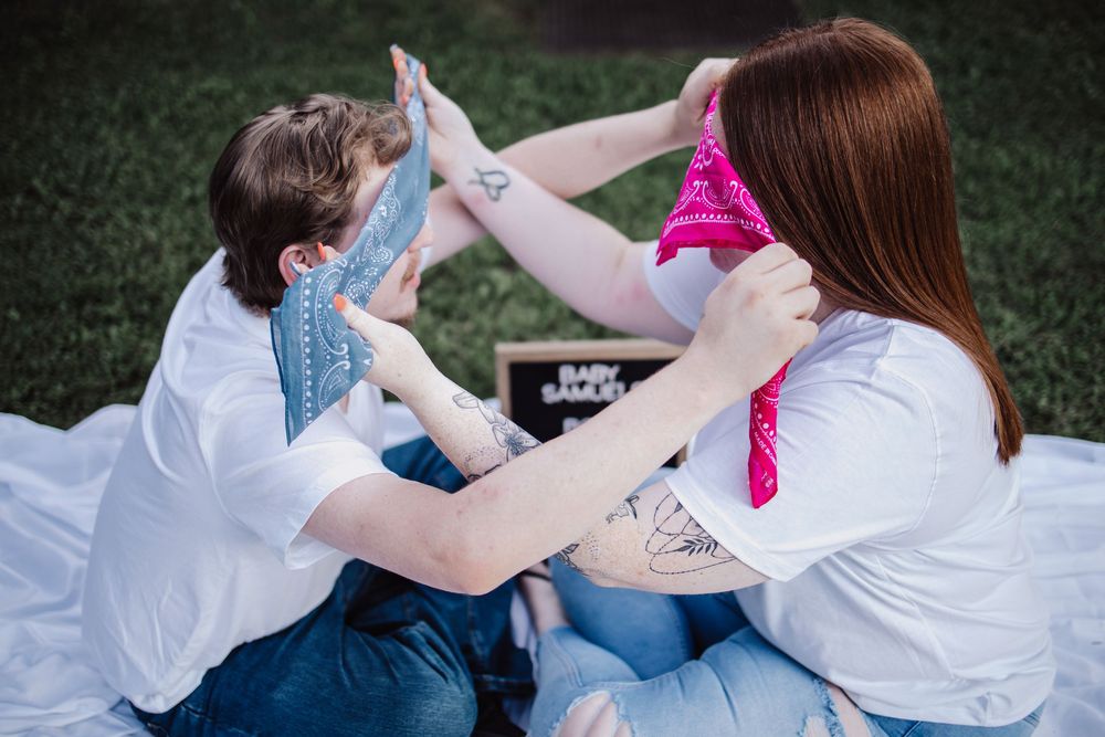 Two people in white shirts high-fiving with pink and blue bandanas during gender reveal celebration.