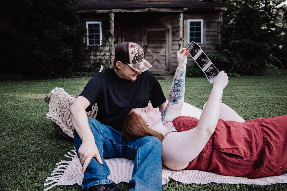 A couple laying on a blanket in front of a rustic house share an intimate moment on the grass.