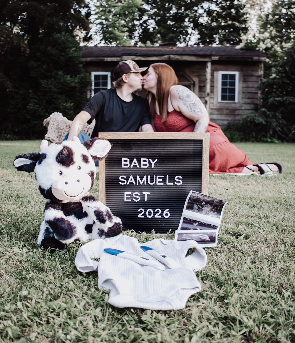 Pregnancy announcement setup with letterboard showing "BABY SAMUELS EST 2026", stuffed cow, and ultrasound photos on grass.
