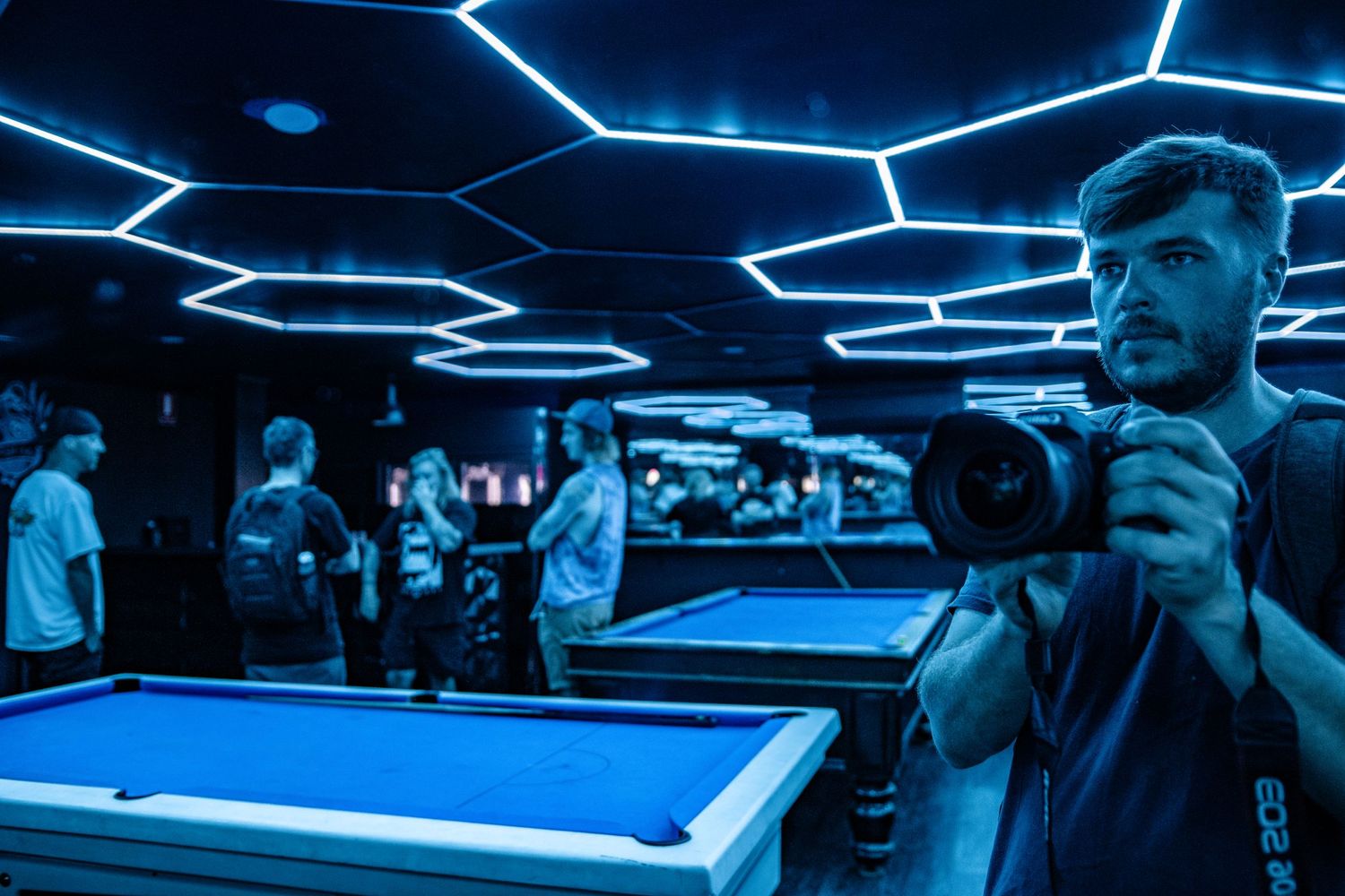 Pool hall interior with neon blue geometric ceiling lights and billiards table.