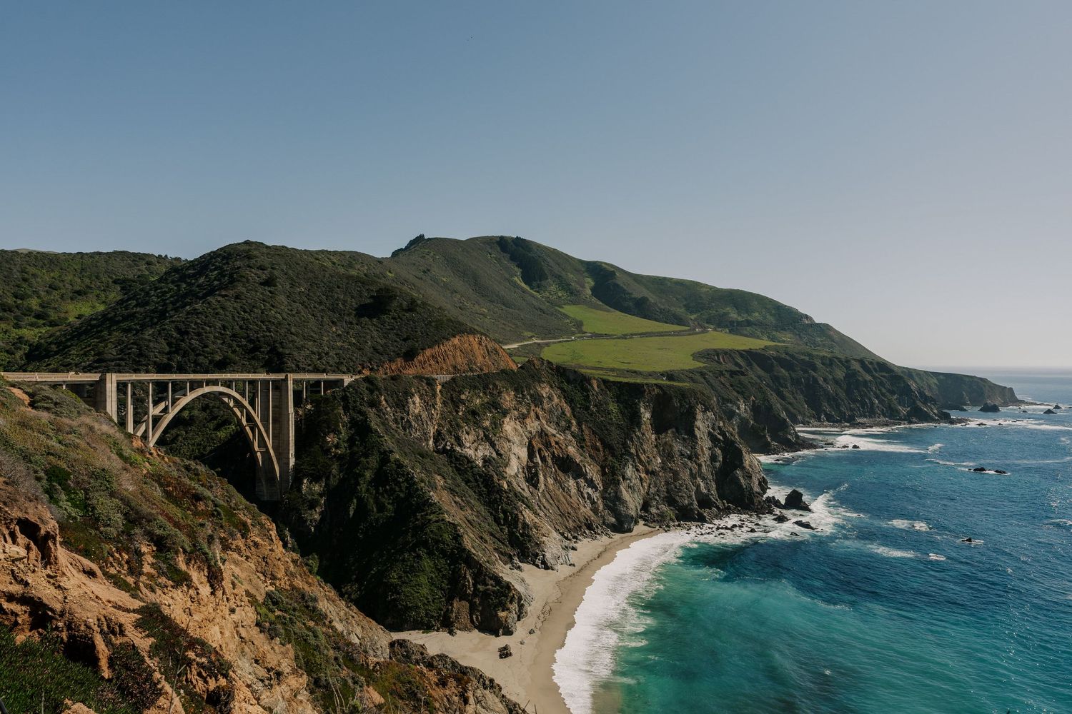 The iconic Bixby Bridge spans across rugged cliffs along California's Big Sur coastline with turquoise waters below.