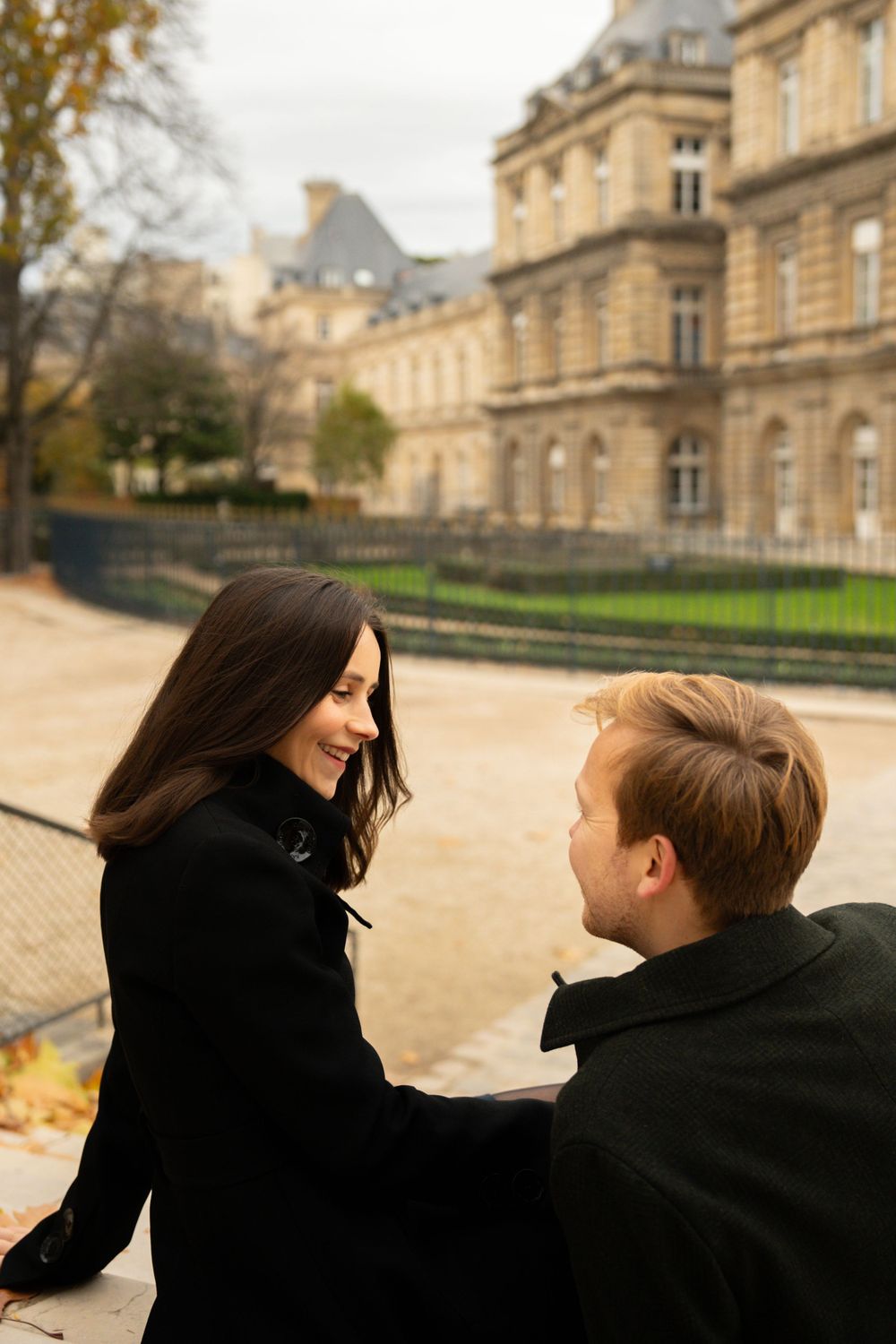 A couple shares a romantic moment together while sitting outside a grand historic building in Paris.