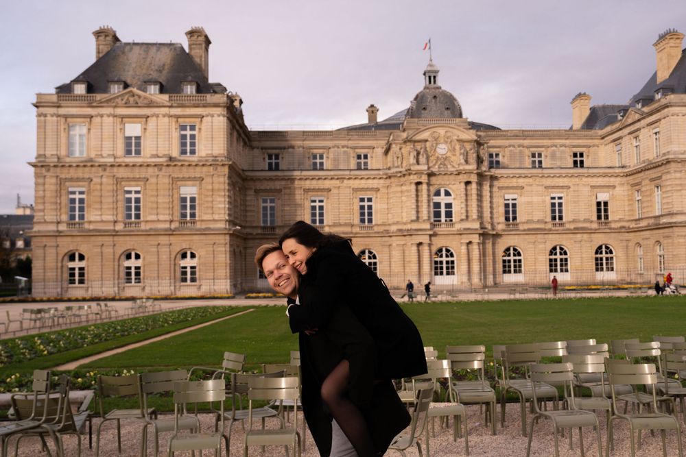 Person poses in front of the historic Luxembourg Palace with outdoor cafe seating in Paris.