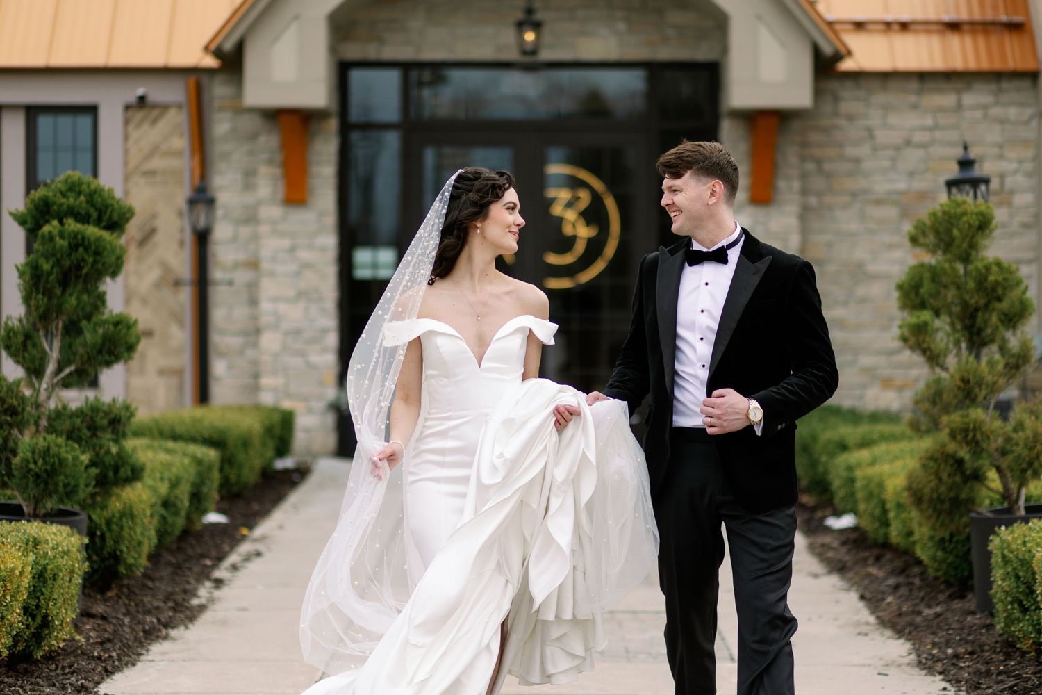 A newlywed couple walks together on a stone path outside the elegant Venue 3Two in Grand Rapids.