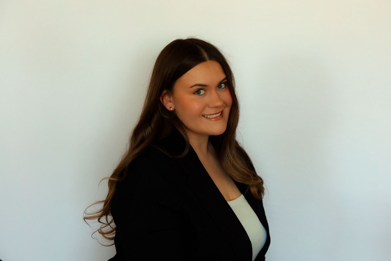 Professional headshot of someone in a black blazer and white top against a light background.