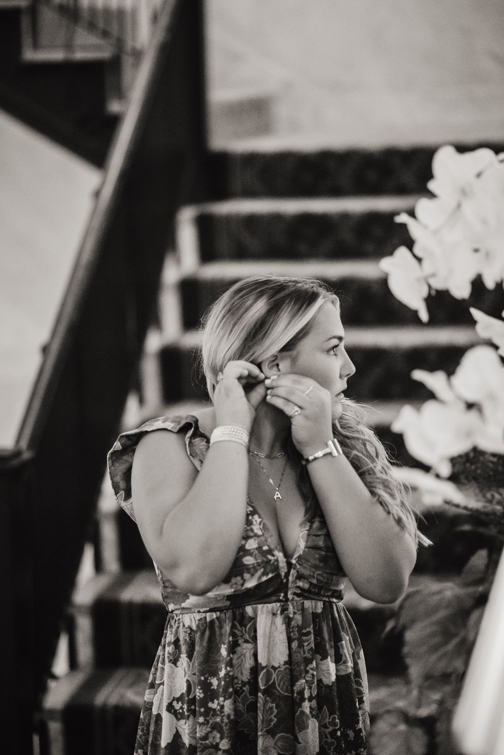 Black and white portrait of person adjusting earrings on staircase.