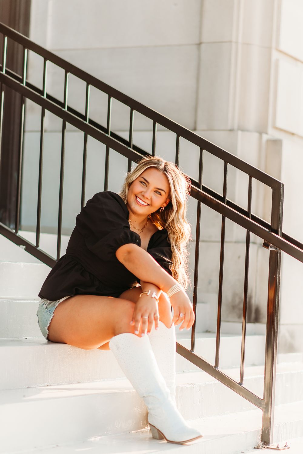 Casual portrait in black top and white boots sitting by modern railing.