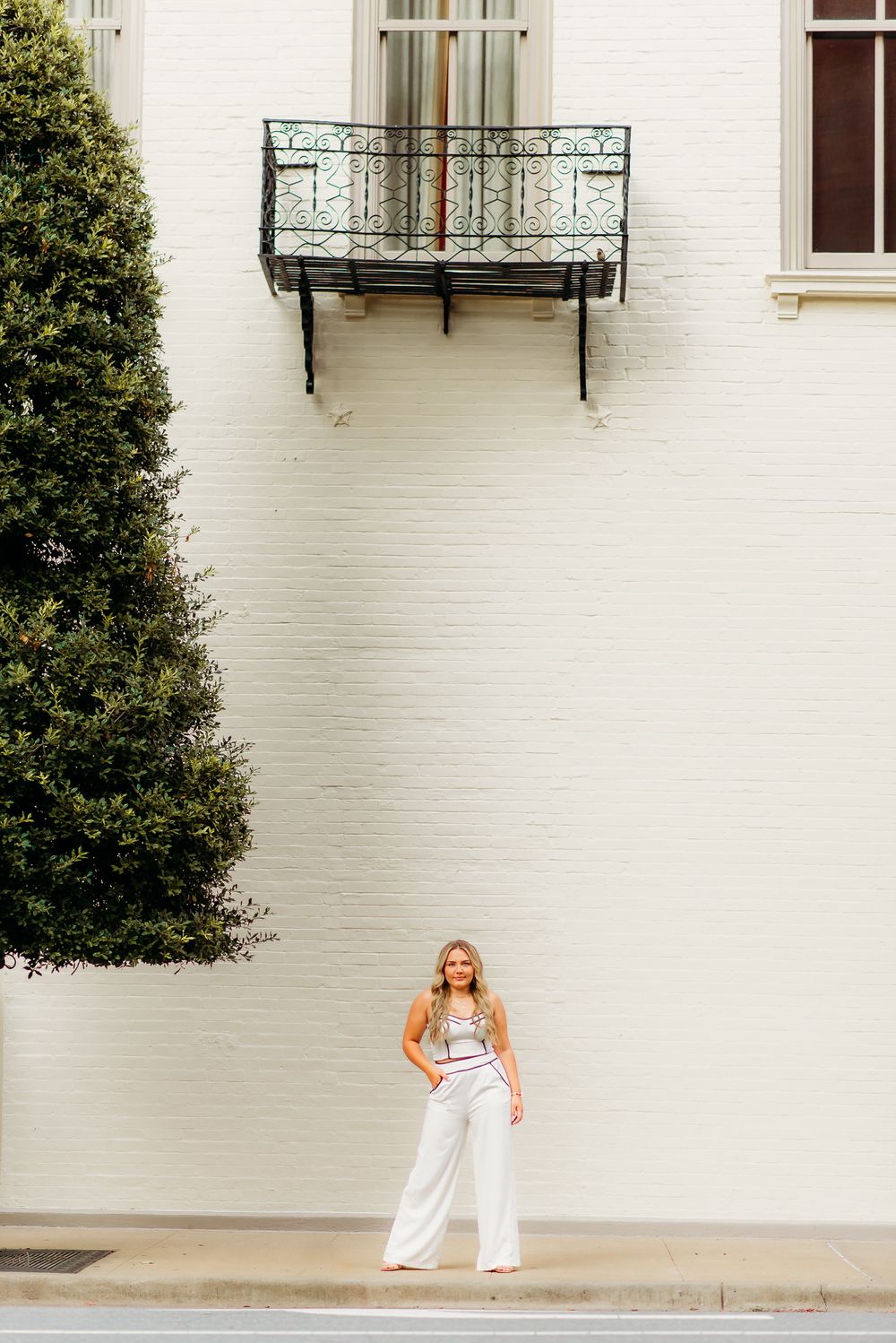 Full length portrait against white building wall with decorative balcony above.