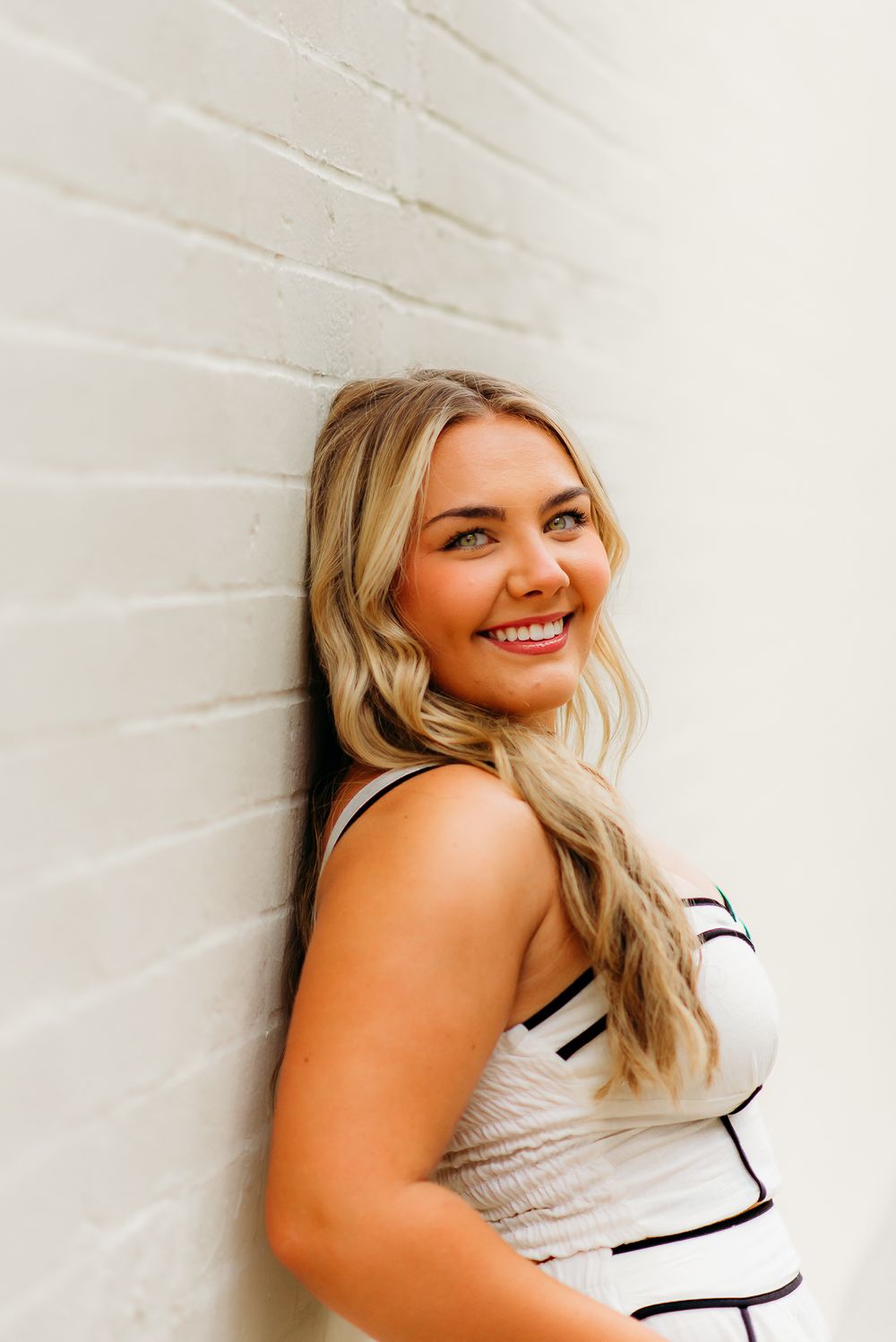 Close up portrait against white brick wall wearing striped summer outfit.